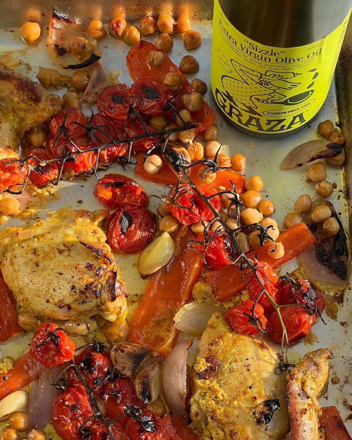 Sheet pan chicken shawarma with blistered tomatoes, chickpeas and peppers, next to a bottle of “Sizzle”