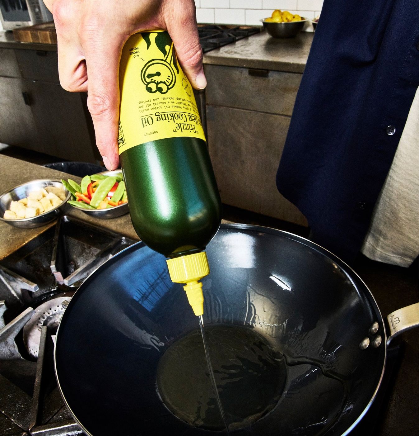 A hand squeezing “Sizzle” into a hot wok